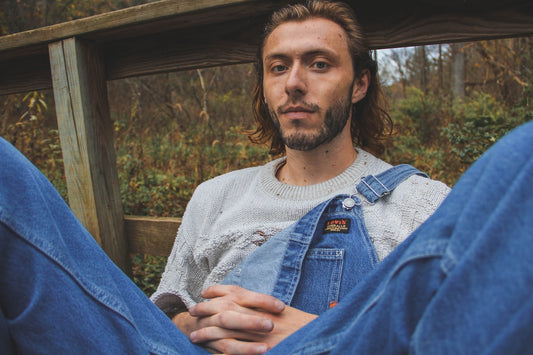 a man with long hair wearing overalls and a sweater