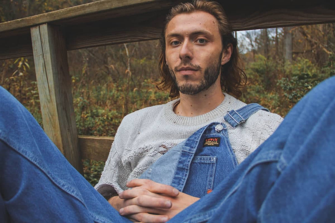 a man with long hair wearing overalls and a sweater