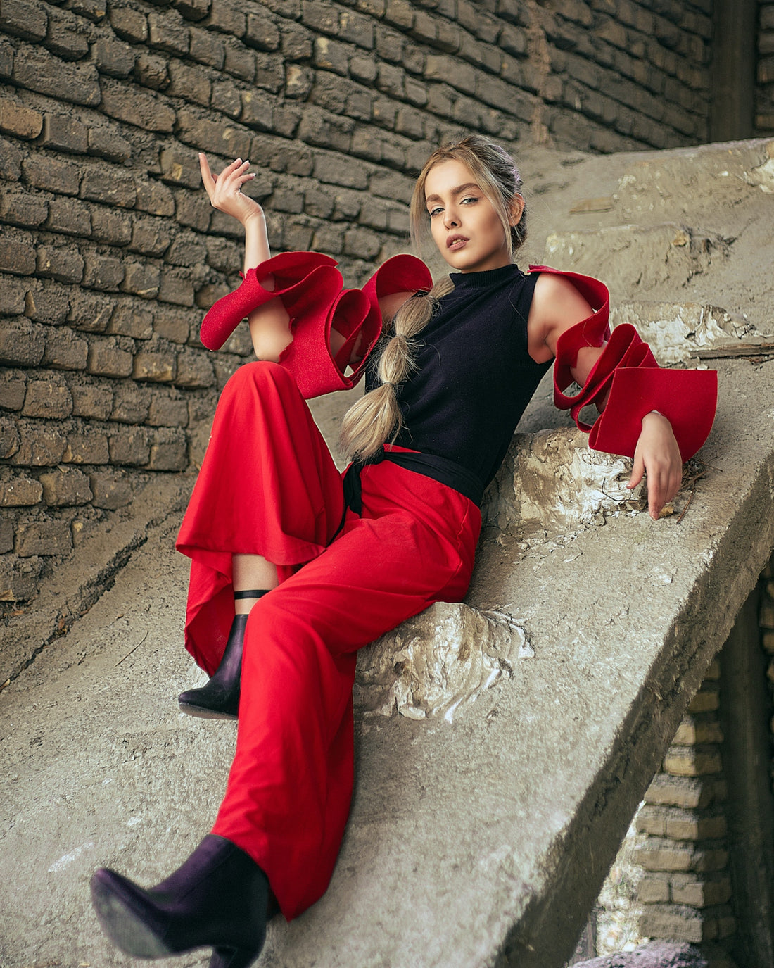 a woman in a black top and red pants sitting on a ledge