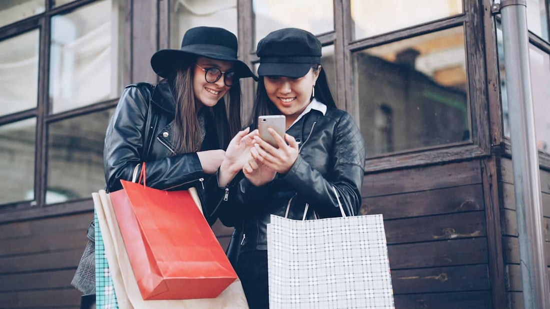 Two women looking at a smartphone with shopping bags.