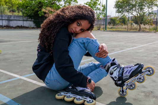Young woman in rollerblades sitting on court