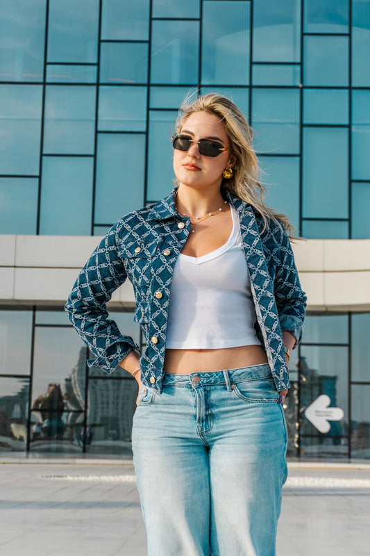 Woman in sunglasses and patterned jacket stands outside.