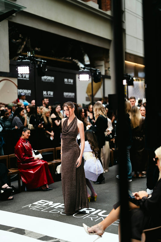 Model walks runway at fashion event with audience.