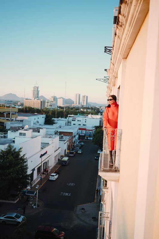 Woman in orange coat on balcony overlooking city street.
