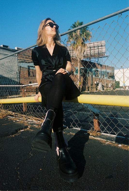 Woman in black sitting on yellow railing outdoors.