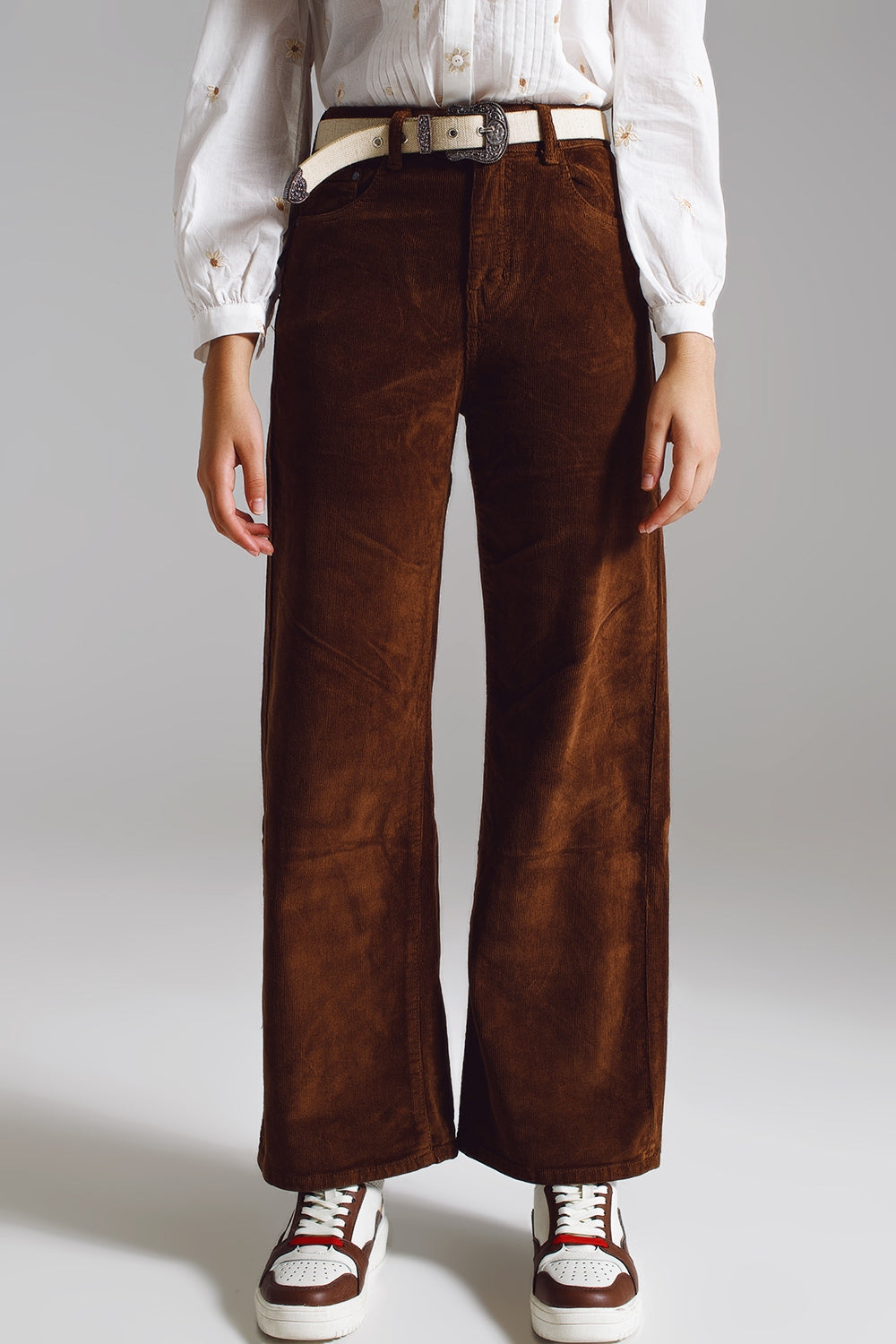 Woman wearing brown corduroy women's trendy trousers paired with white belt and shirt