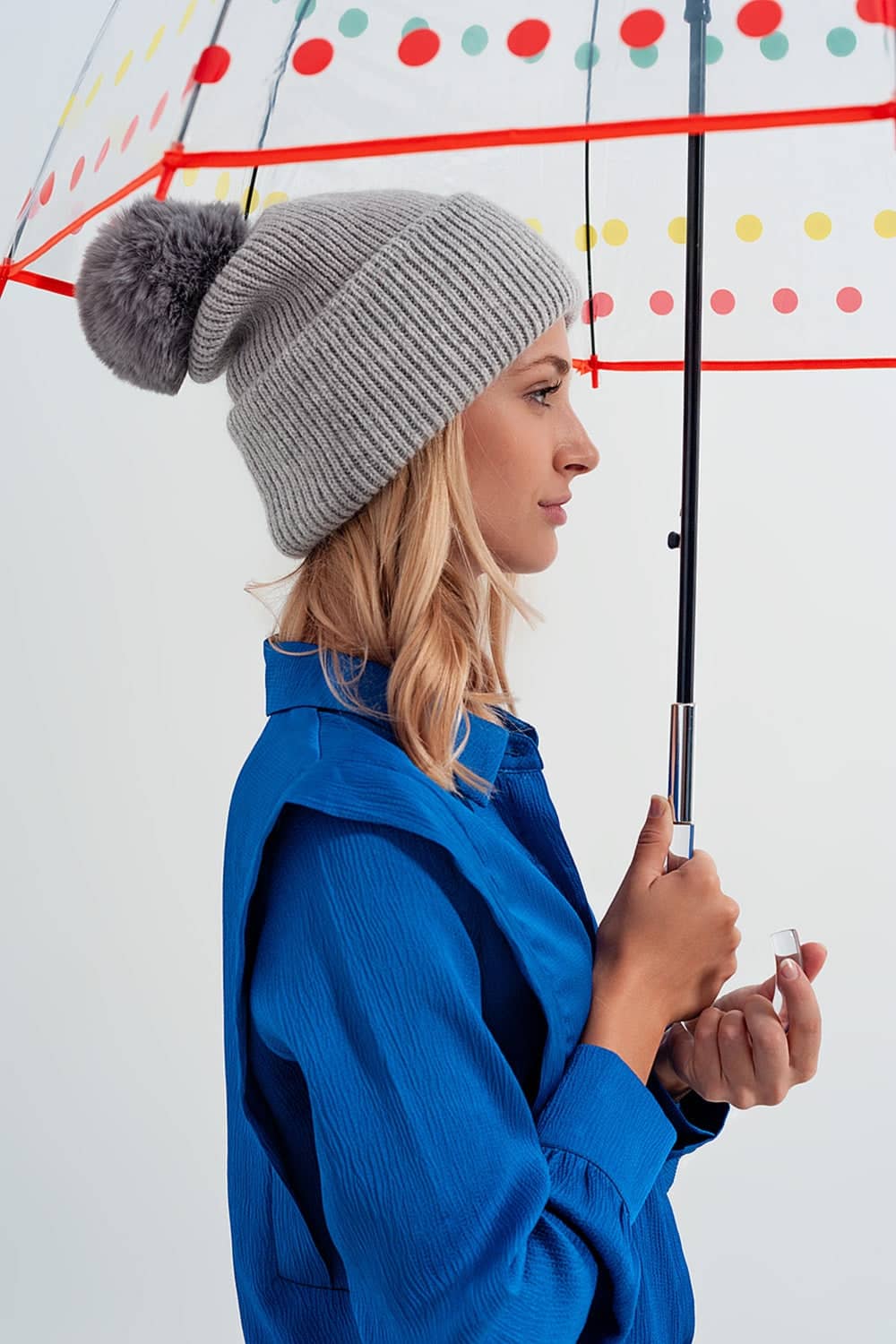 Woman wearing trendy accessories for women including a grey pom pom hat holding a colourful umbrella
