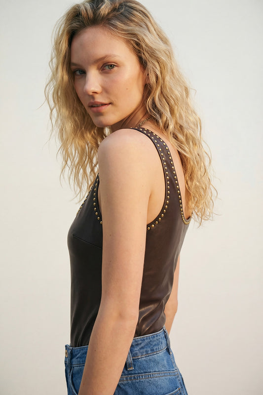 Woman wearing a brown faux leather bodysuit with stud detail, styled with denim jeans.