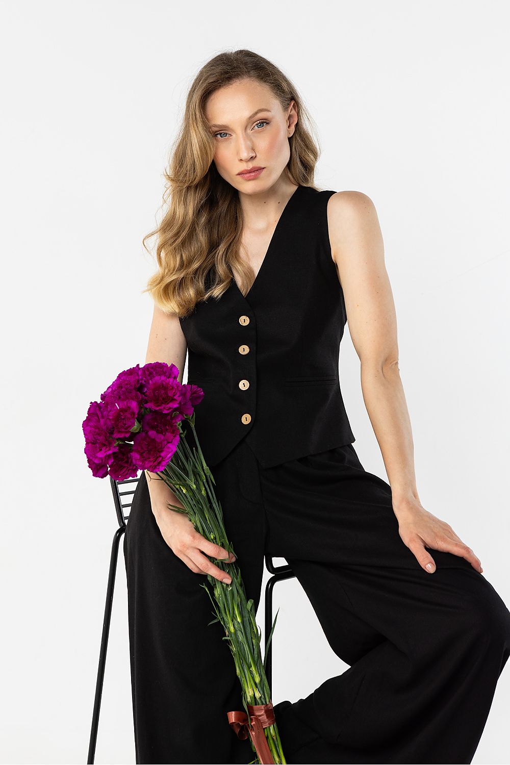 Elegant black gilet by Awama with wooden buttons, styled with wide trousers and flowers