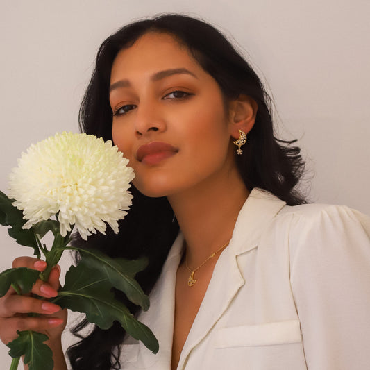 Luna Charles gold earring earrings showcased by a model holding a white flower in a stylish outfit